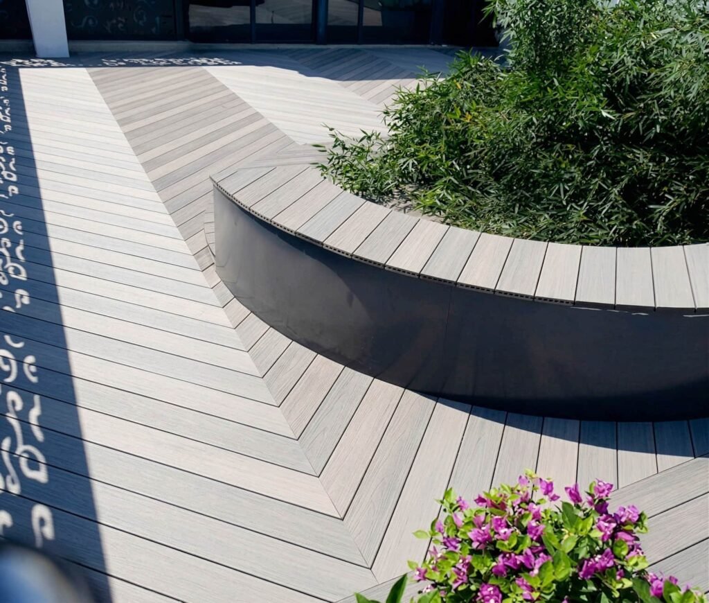 Outdoor seating area with curved planter and grey composite decking around plants.