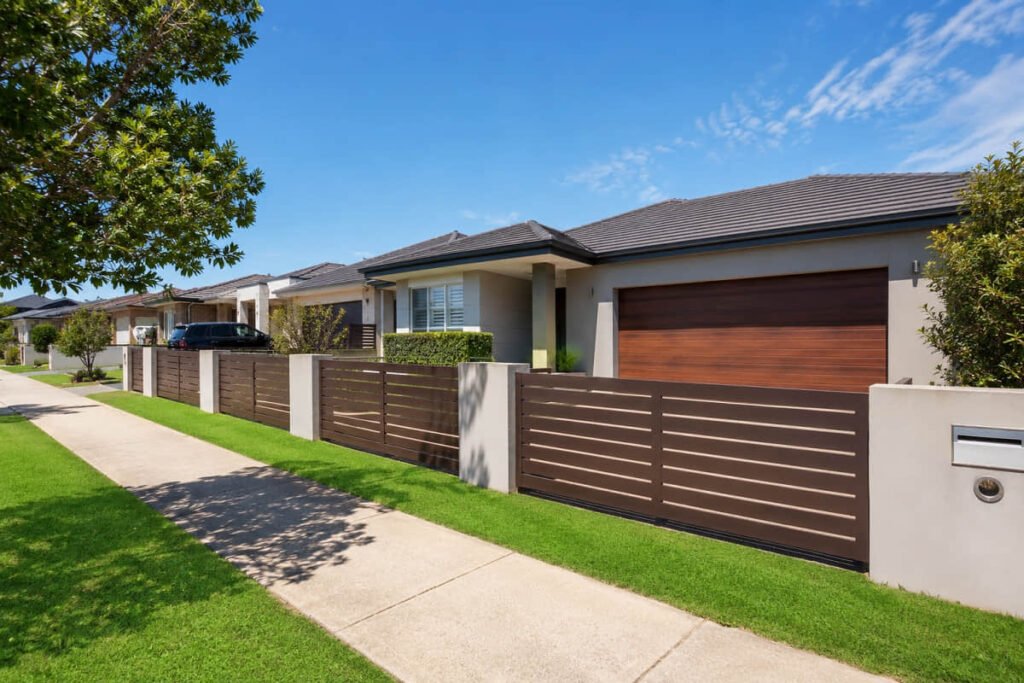 A suburban front yard with houses and a continuous composite screening fence by the footpath
